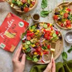 Drei Teller mit Orzo-Salat, bunt belegt mit Gemüse und gewürzt mit dem Bio Tomaten Food Finisher, dessen Verpackung gut sichtbar im Bild liegt.