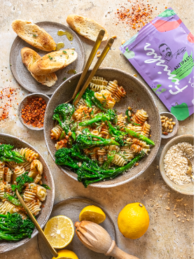 Zwei Schalen mit Nudeln, Brokkolini, Pinienkernen und Zitronensauce, daneben geröstetes Brot, Parmesan und die Verpackung des Bio Antipasti Food Finishers.